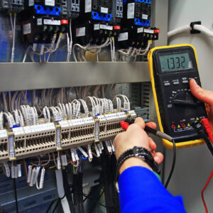 engineer tests the industrial electrical circuits with a multimeter in the control terminal box. Engineer's hands with a multimeter close-up against background of terminal rows of automation panel.
