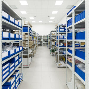 Warehouse of components for the electronics industry. White metal racks with blue plastic trays and cardboard boxes installed in them.